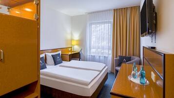 Ein Hotelzimmer mit Doppelbett, Schreibtisch mit Stuhl, Wandfernseher und einem Vorhangfenster.