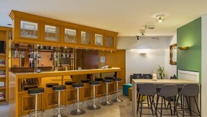 A bar area with wooden cabinets, multiple stools, and a counter with bar tools. - Aspire Frankfurt Airport, Trademark Collection by Wyndham (Ruesselsheim)