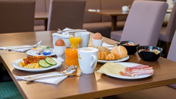 A breakfast table with plates of food, a coffee cup, and a glass of orange juice. - Aspire Frankfurt Airport, Trademark Collection by Wyndham (Ruesselsheim)