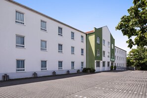 A modern building with a white facade and a green section, featuring multiple windows and a paved courtyard. - Aspire Frankfurt Airport, Trademark Collection by Wyndham (Ruesselsheim)