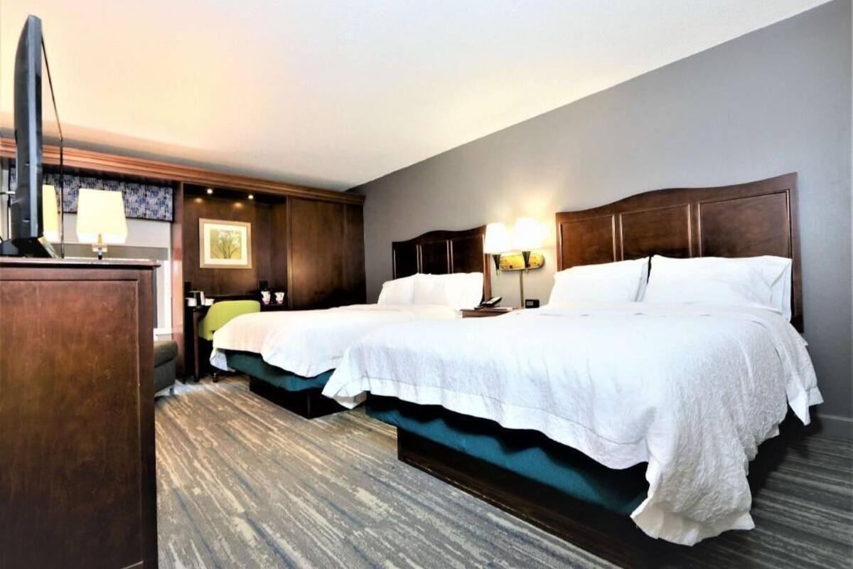 A hotel room with two beds, a desk, and a TV.