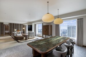 Ein geräumiges Hotelzimmer mit großem Esstisch, bequemen Sitzgelegenheiten, einem Fernseher und Blick auf die Stadt.