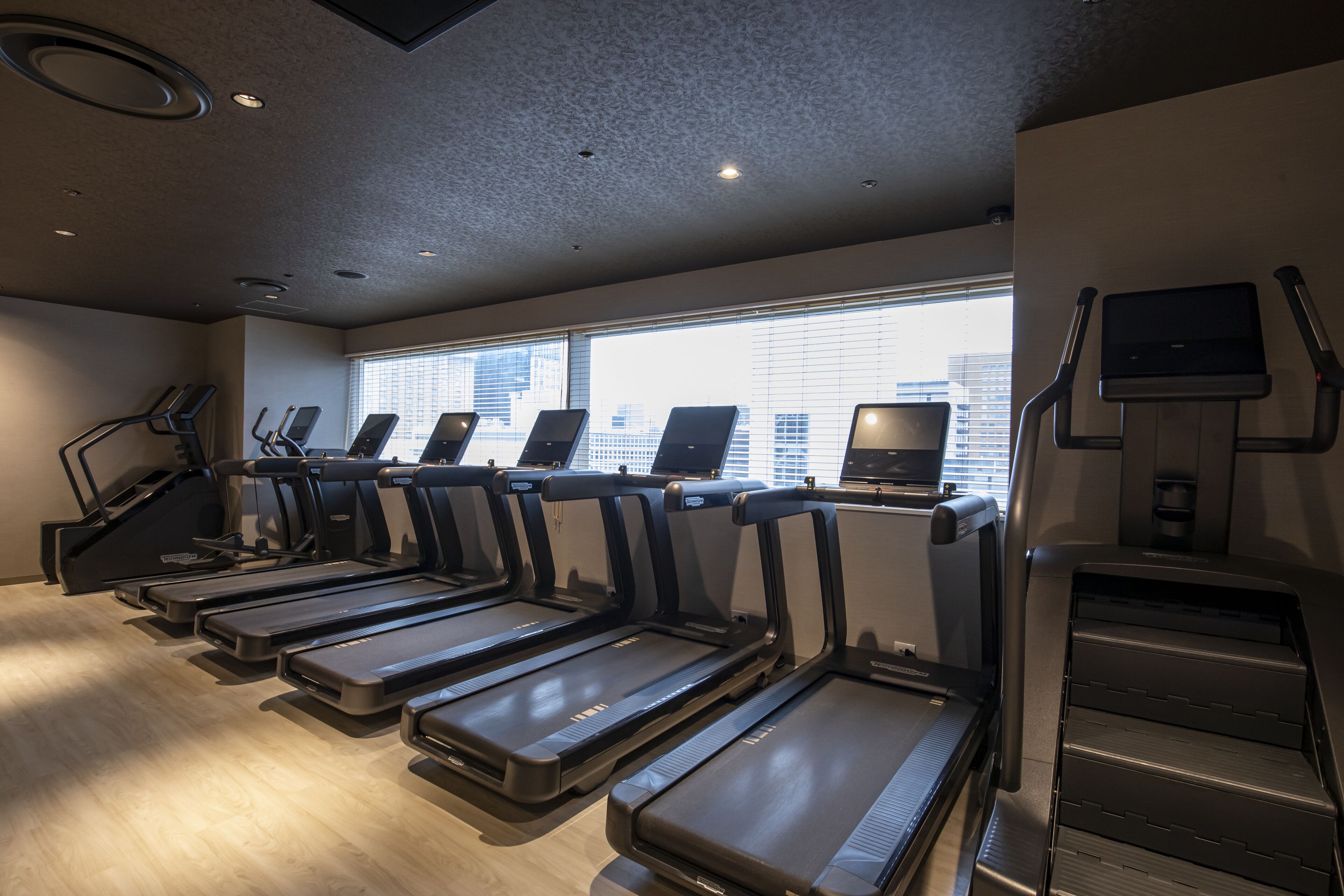 A gym with treadmills, a stair climber, and a television on a wall.