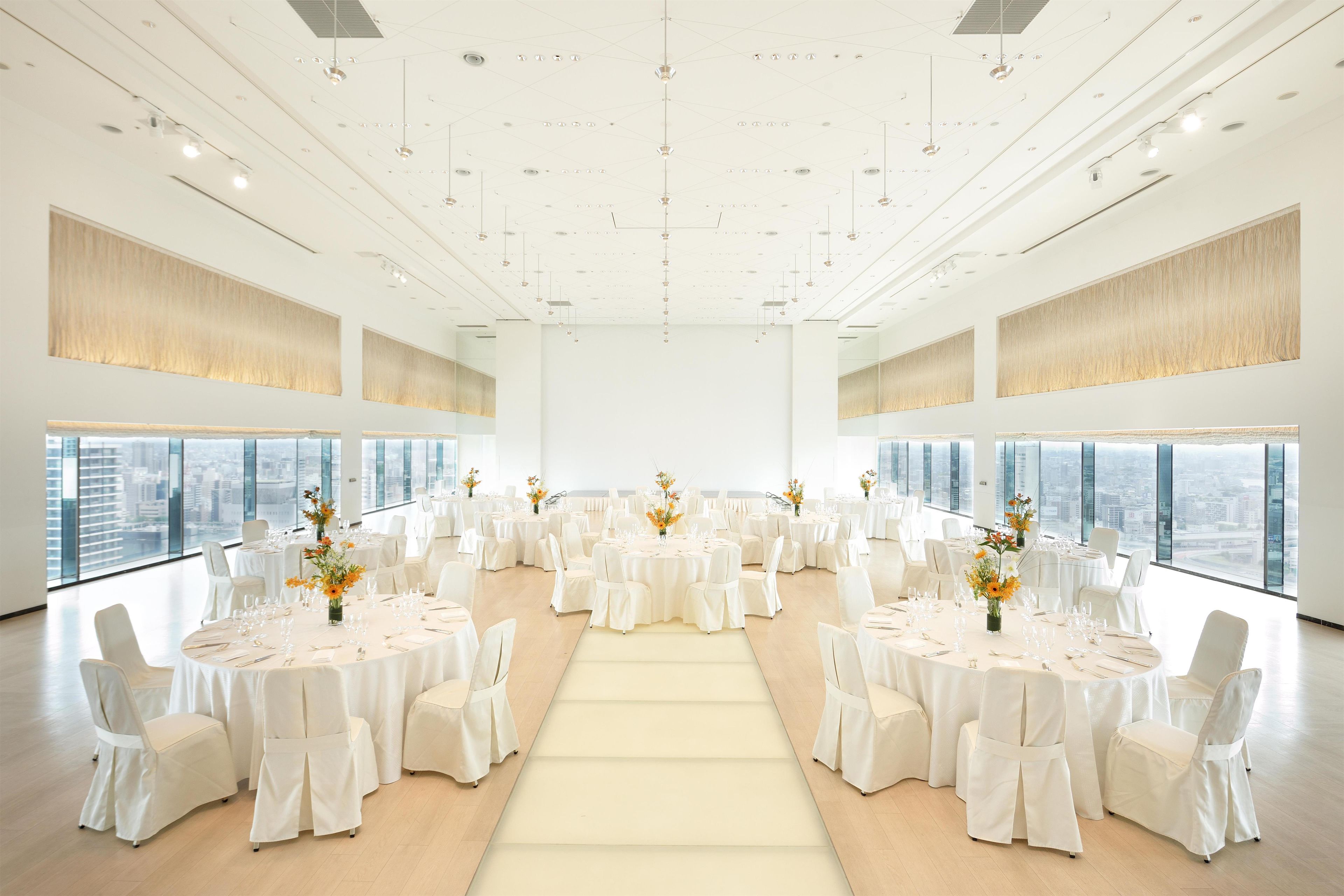 A spacious conference room with round tables, white chairs, and large windows offering a city view.
