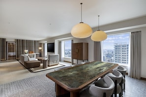 Une chambre d’hôtel moderne dotée d’un coin repas, de sièges confortables, d’une grande fenêtre offrant une vue sur la ville et d’un téléviseur.