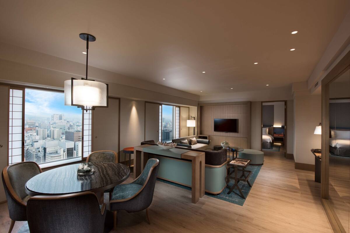 A modern hotel room with a dining area, a living space, and a view of the city.