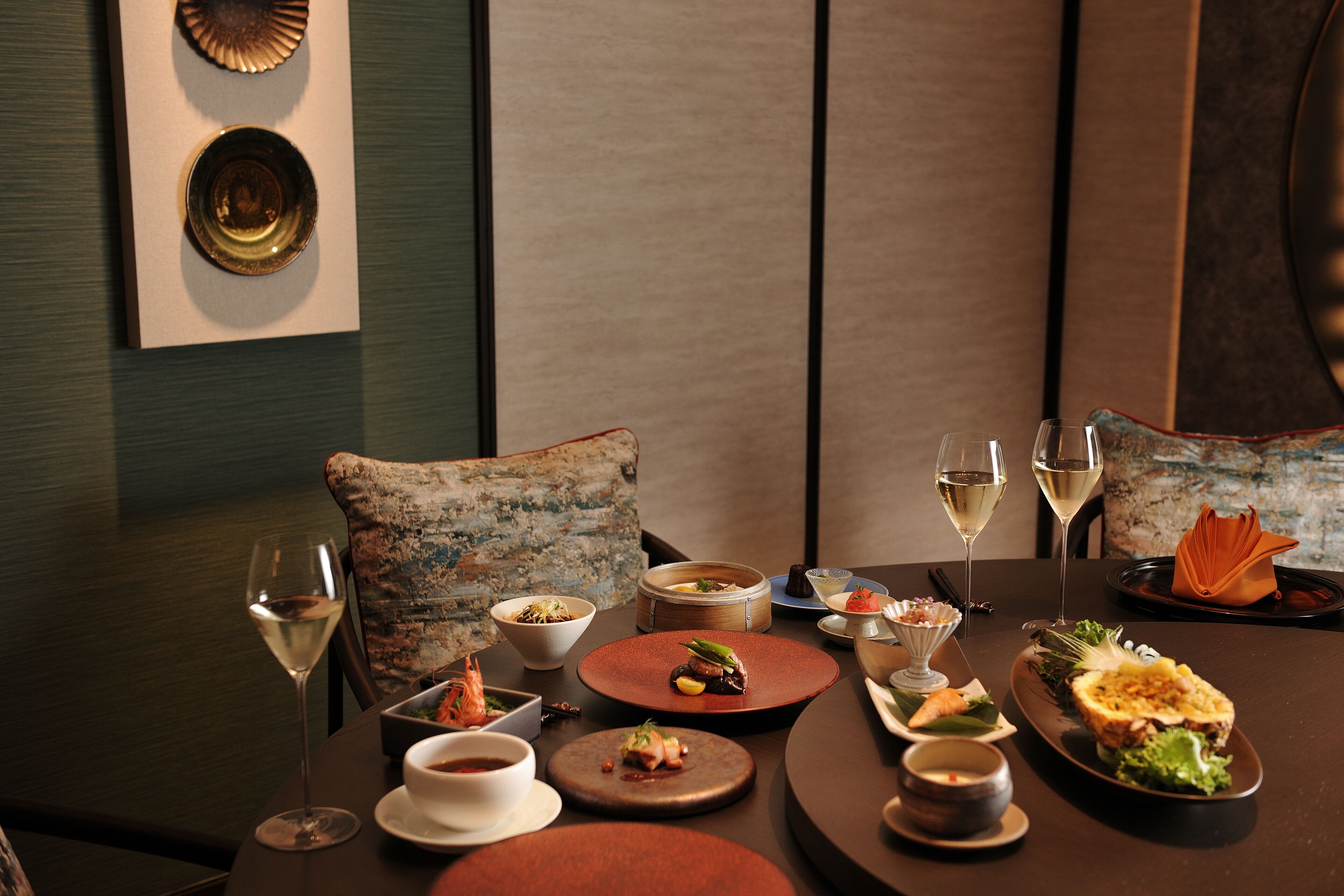 A dining table set with various dishes, glasses of wine, and a decorative pillow.