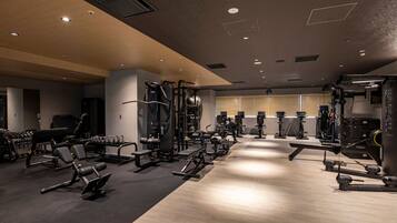 A modern gym with various exercise equipment, a wooden floor, and a large window with blinds.