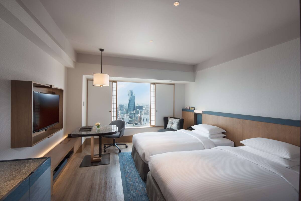 A hotel room with a large TV, a desk, two beds, and a city view.