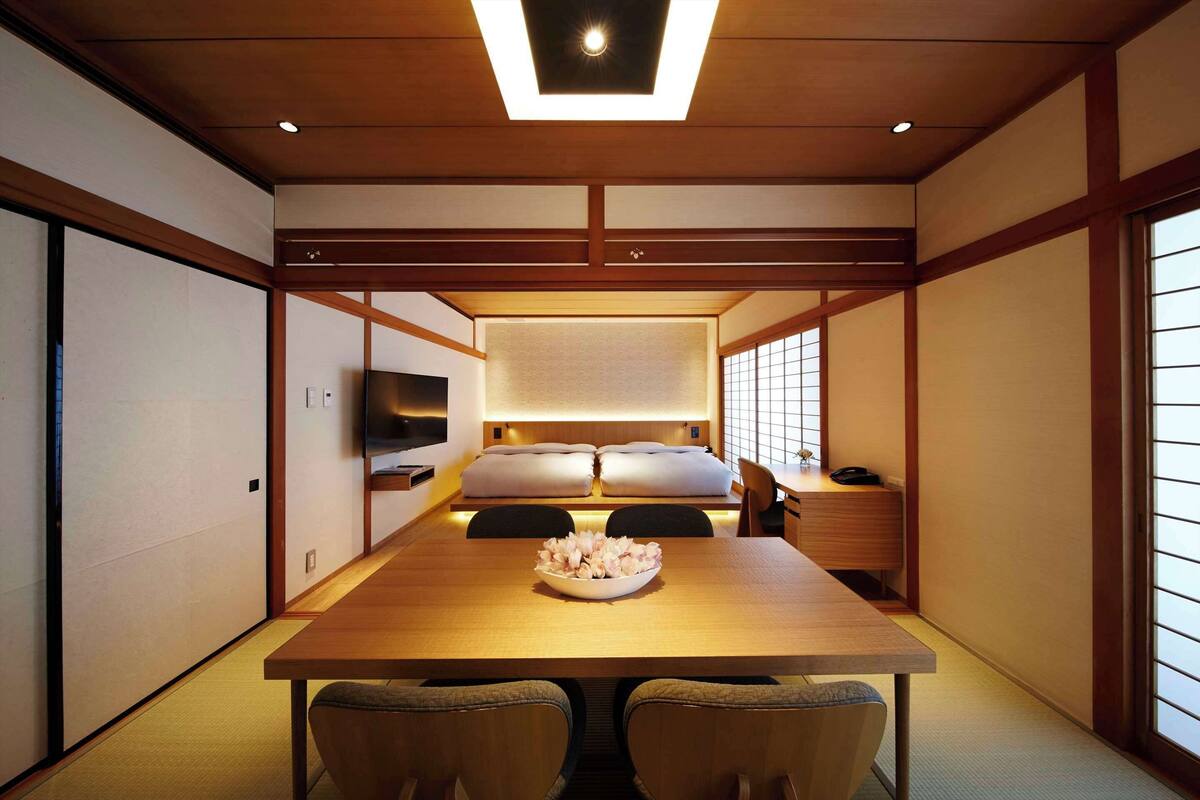 A traditional Japanese-style room with tatami flooring, a low wooden table, and a bed with pillows.