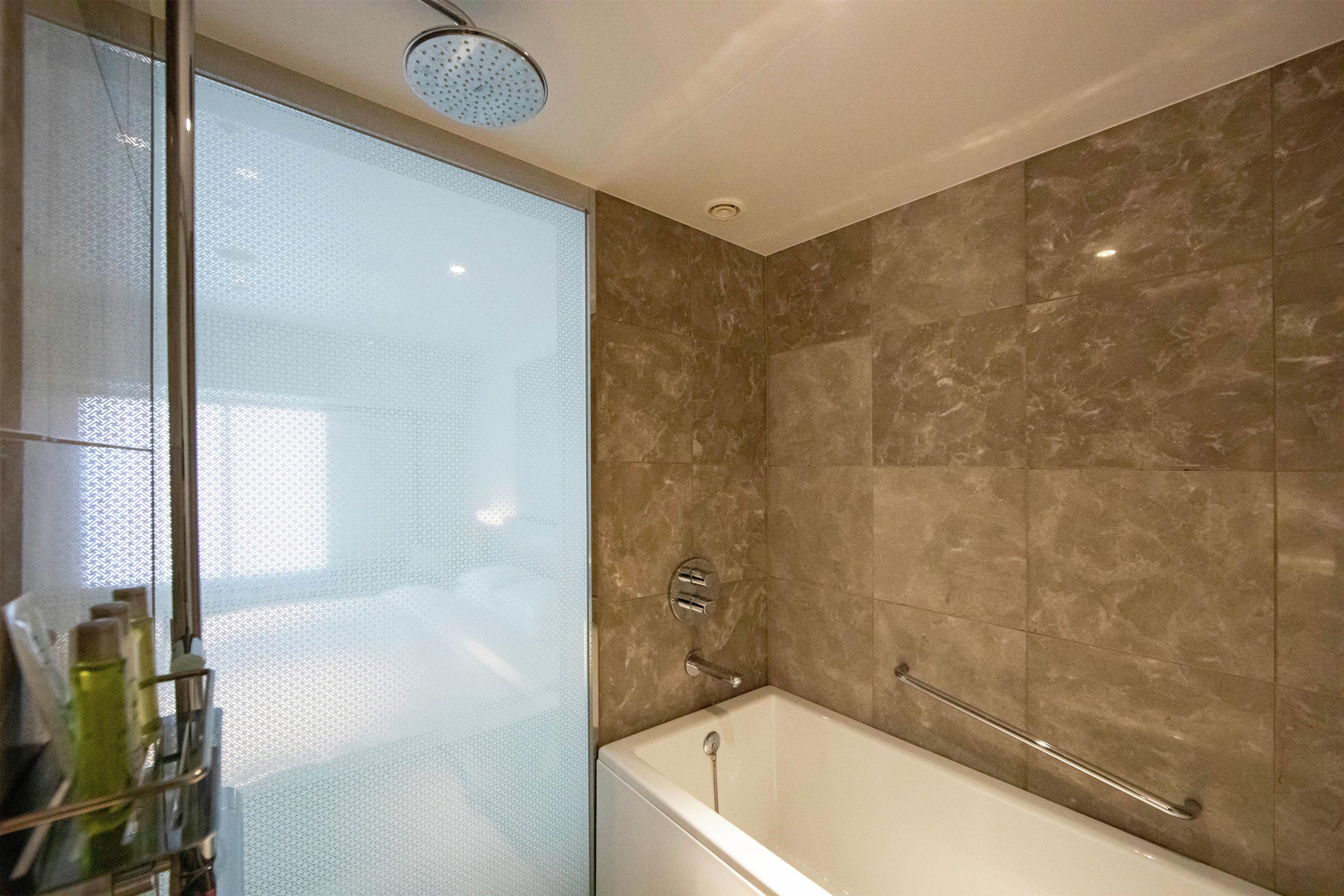A bathroom with a glass shower enclosure, a bathtub with a grab bar, and marble walls.