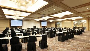 A conference room with rows of tables and chairs, a large screen, and a chandelier.