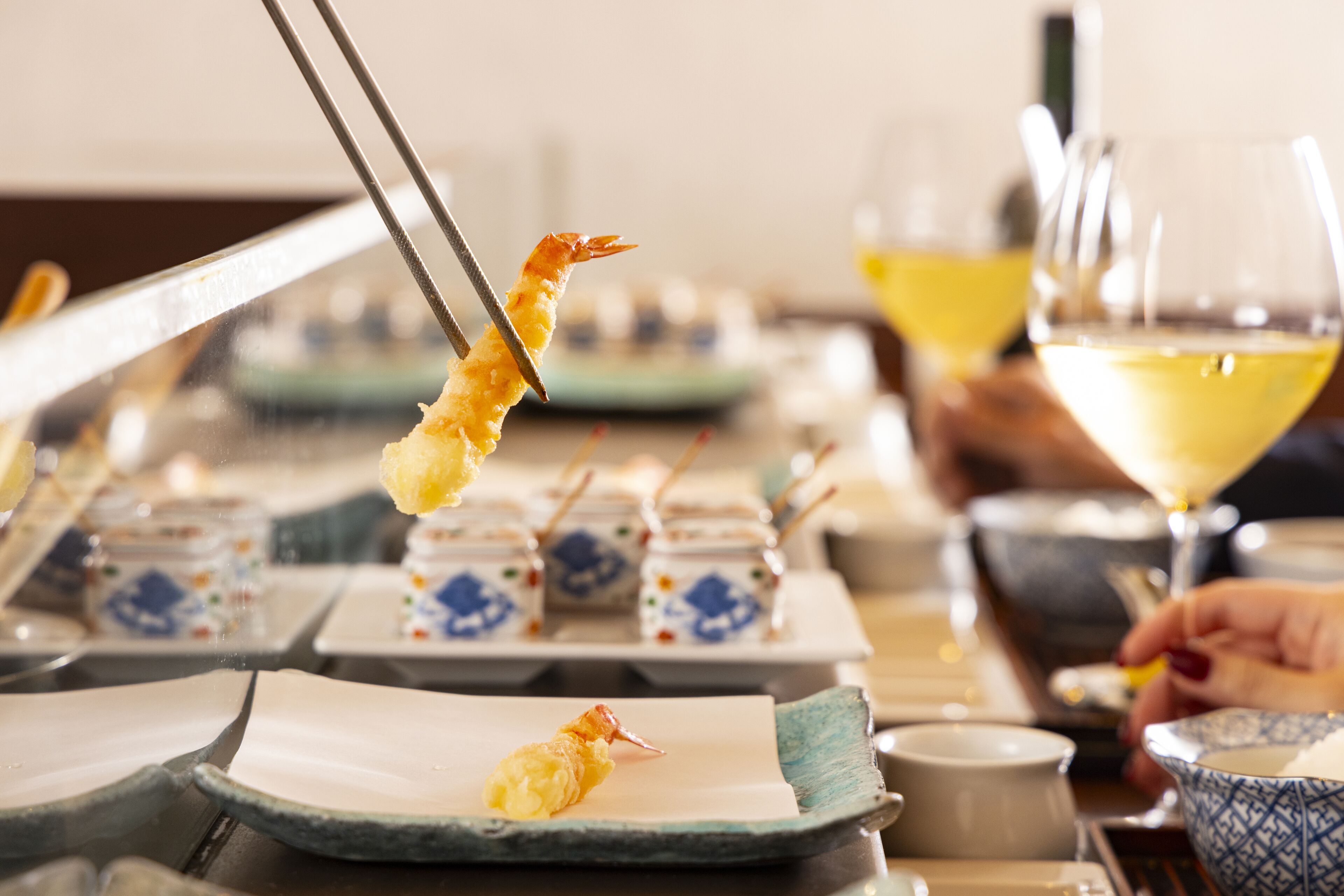 A dining table with plates, a glass of wine, and a person holding a fork with food.