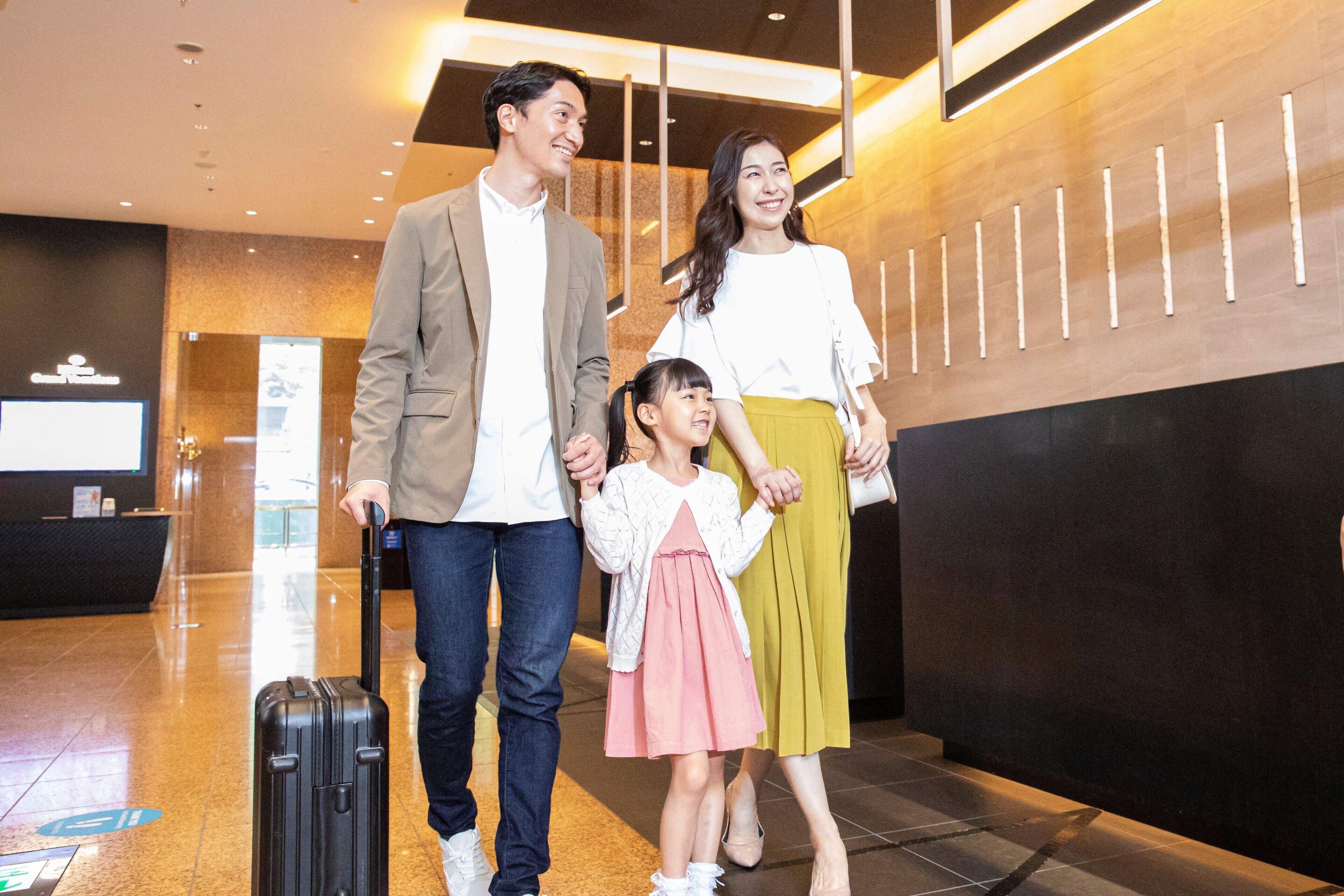 A family walking through a modern lobby with a reception desk and a digital screen in the background.