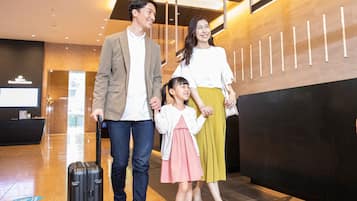 A family walking through a modern lobby with a reception desk and a digital screen in the background.