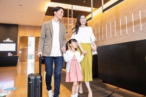 Una familia caminando por un vestíbulo moderno con una recepción y una pantalla digital al fondo.