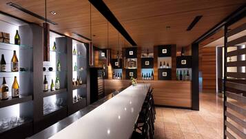 A modern bar area with a long counter, shelves with bottles, and a wooden ceiling.