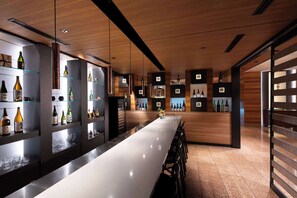 A modern bar area with a long counter, shelves with bottles, and a wooden ceiling.