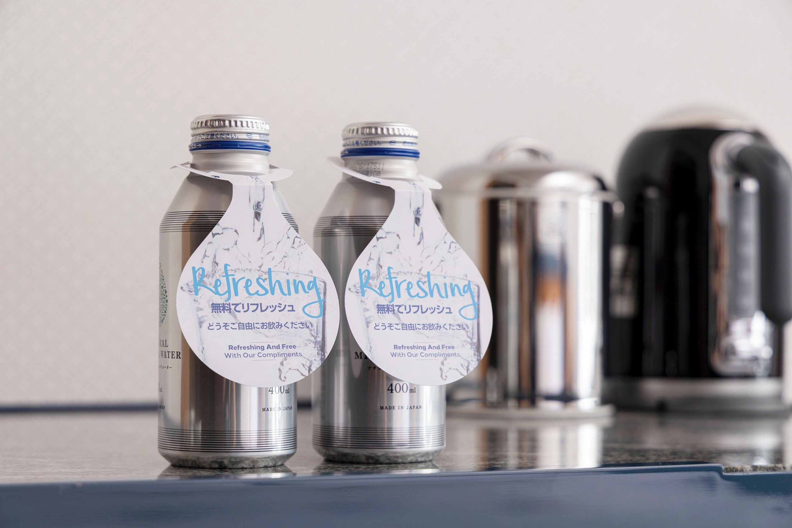 Two stainless steel water bottles with labels, a kettle, and a coffee maker on a countertop.