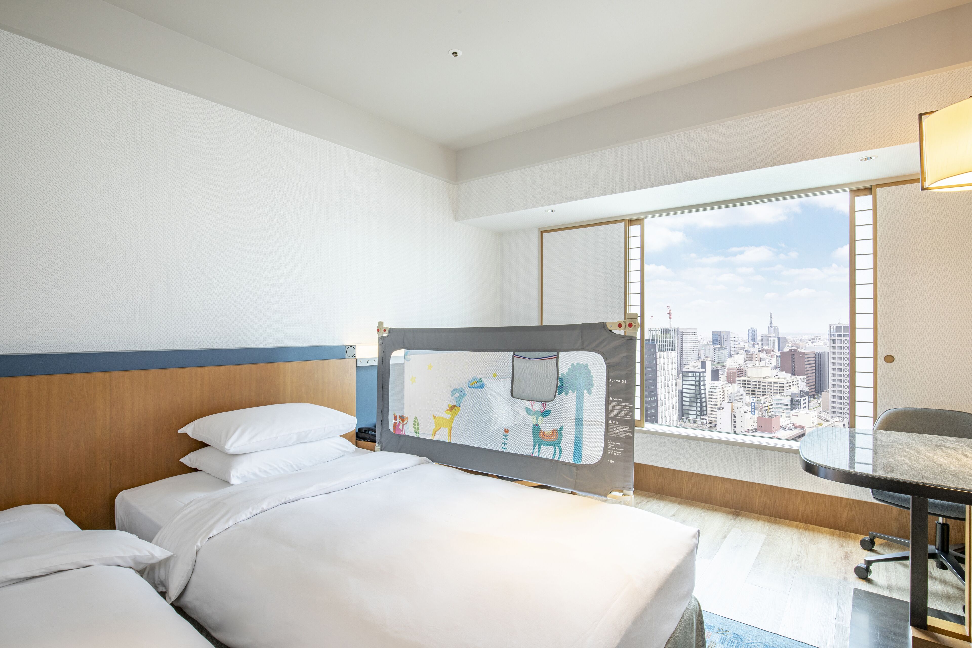 Quarto de hotel com uma cama grande, uma escrivaninha e vista para a paisagem urbana através de uma janela ampla.