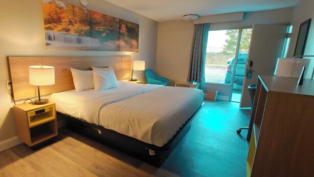 Une chambre d’hôtel avec un lit, des lampes de chevet, un bureau, une chaise et une grande fenêtre.