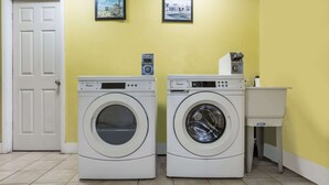 Une buanderie équipée de deux machines à laver et deux sèche-linge à chargement frontal, une porte blanche et deux tableaux encadrés accrochés au mur.