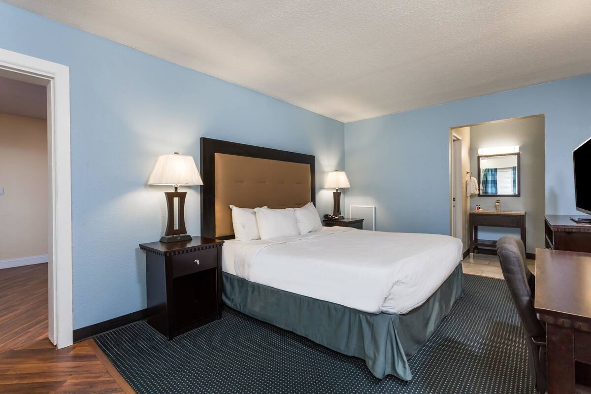 A hotel room with a bed, two bedside tables with lamps, a desk, a chair, and a mirror.