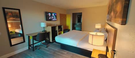 A hotel room with a bed, desk, chair, TV, and a mirror.