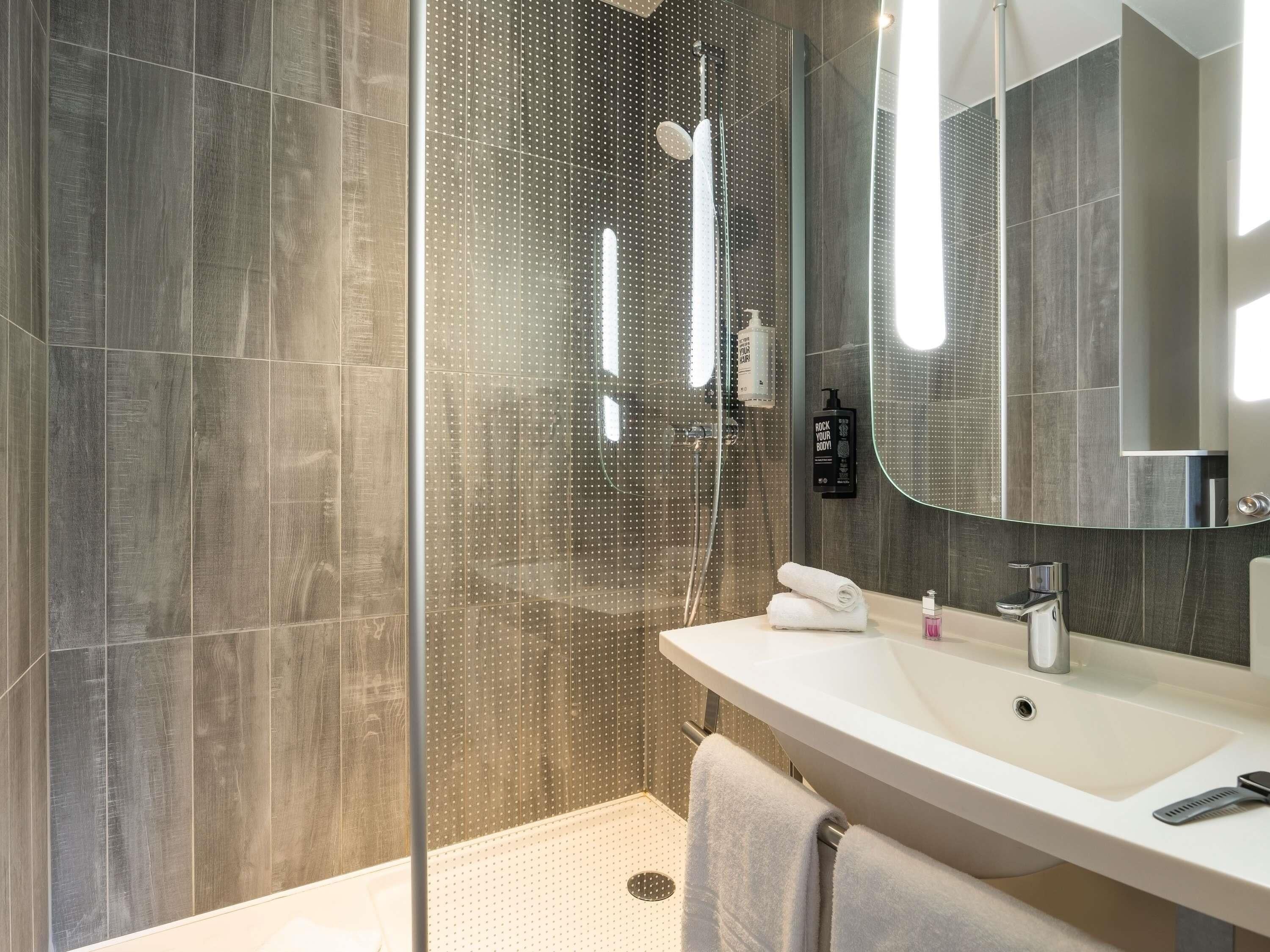 A modern bathroom with a glass shower enclosure, a white sink, and a large mirror.
