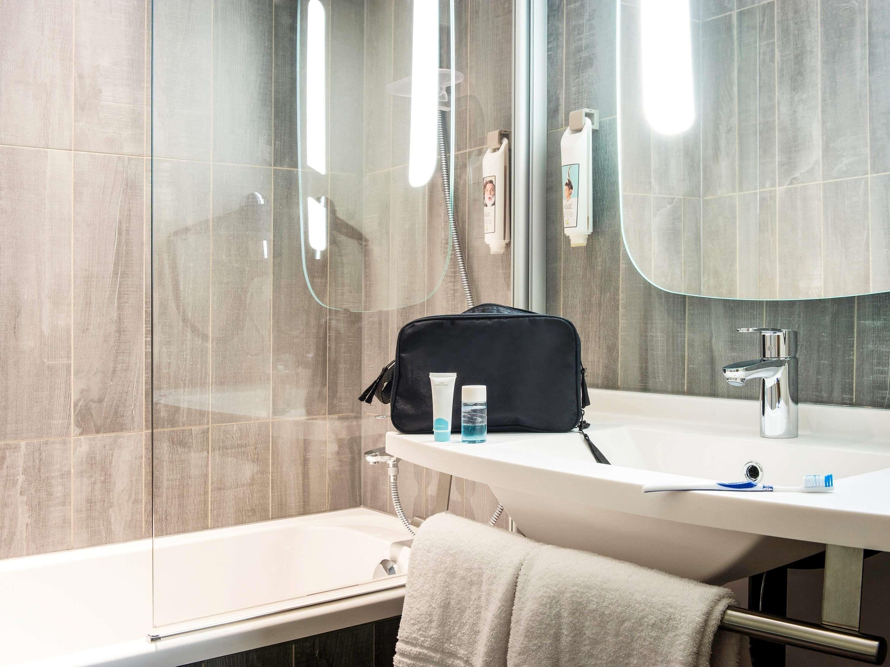 Un baño moderno con cabina de ducha de vidrio, un lavamanos blanco con espejo y un perchero.