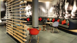 Een moderne zithoek met een houten lambrisering, een grijze bank met rode kussens, en een rode fauteuil.