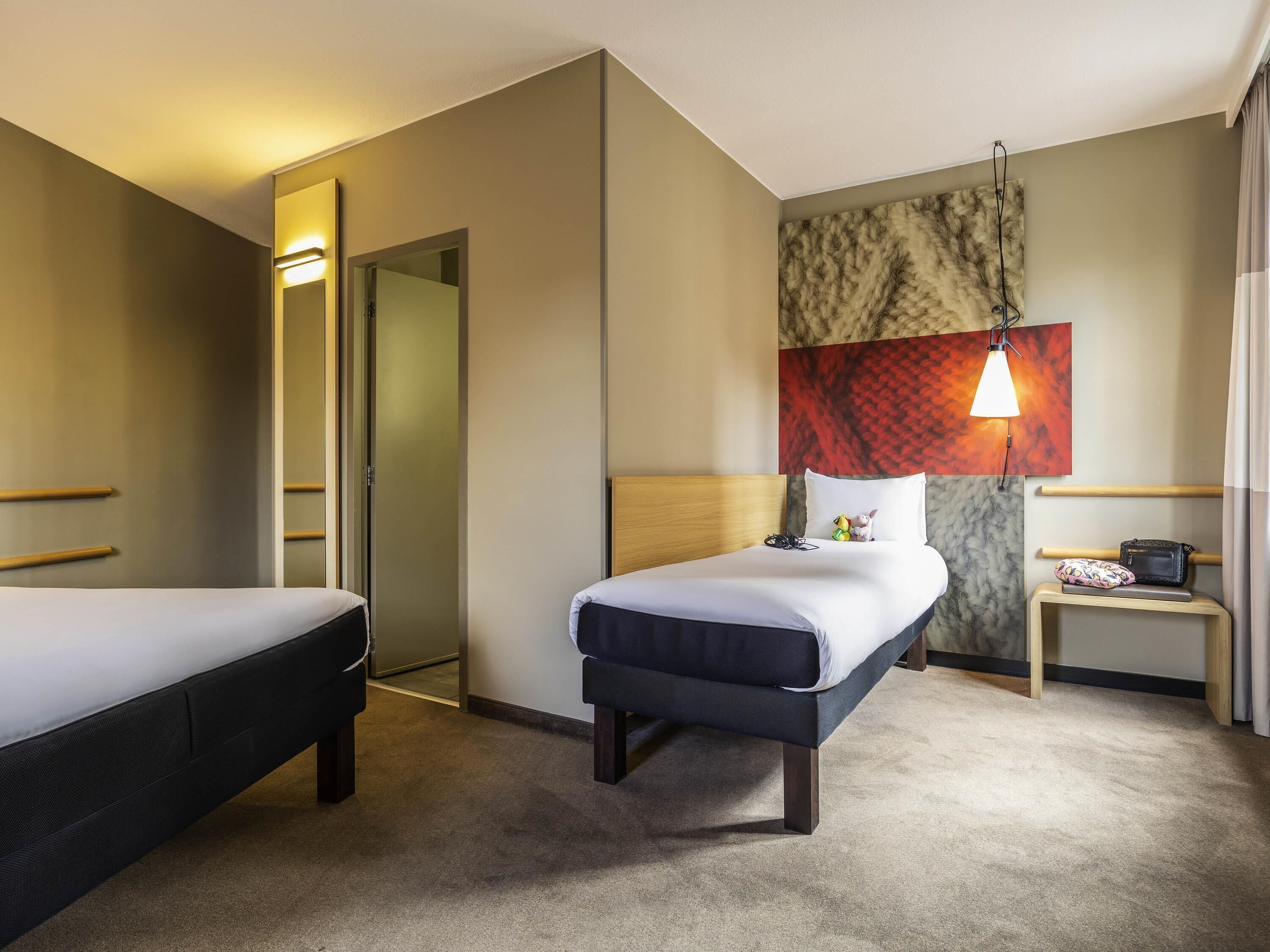 Habitación de hotel con dos camas, una mesita de noche, una lámpara y una pared con textura.