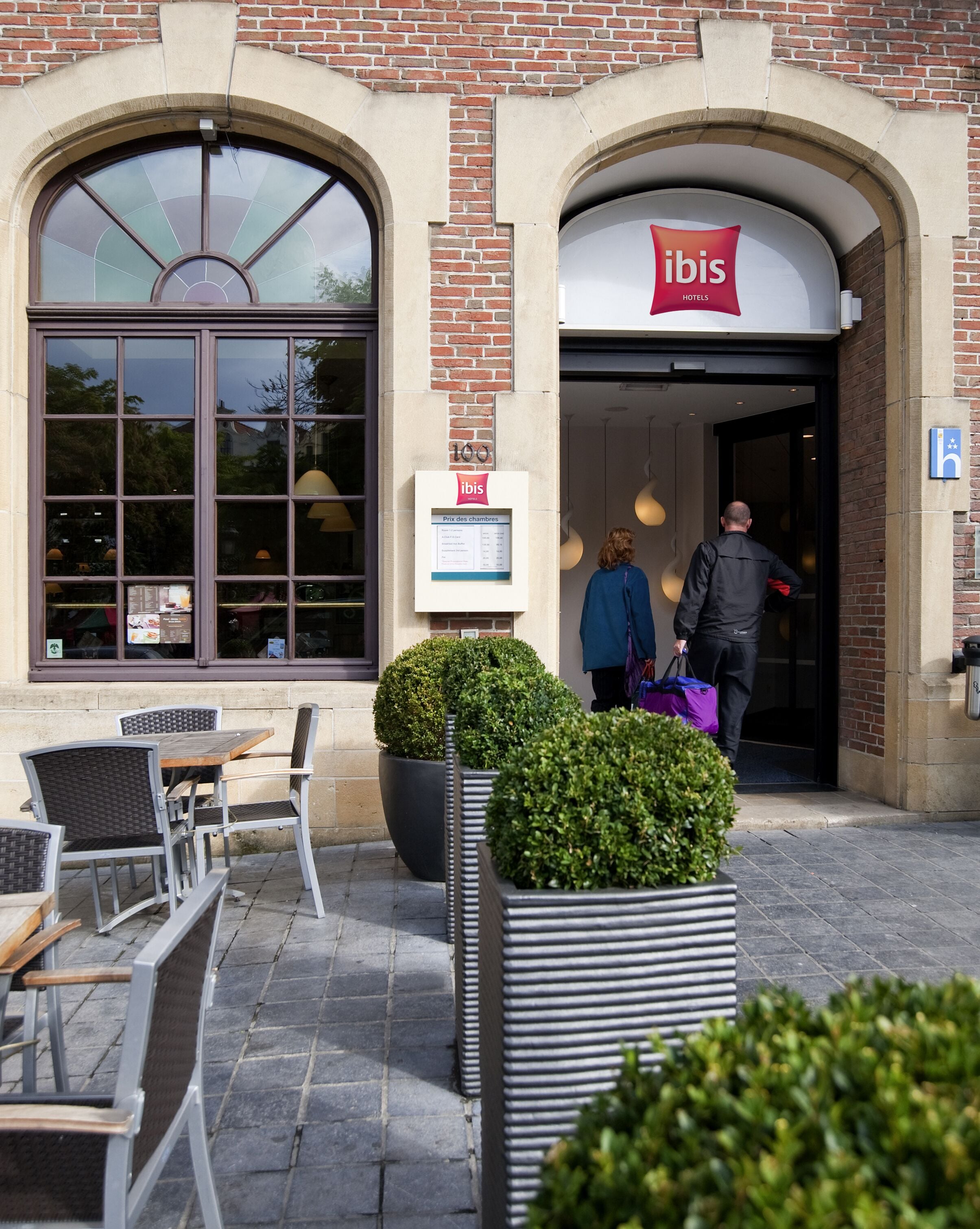 An exterior of an ibis hotel with a brick facade, large windows, and outdoor seating area.