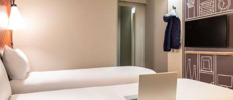 Una habitación de hotel con dos camas, una laptop sobre una cama, un televisor en la pared y un abrigo colgado en la pared.