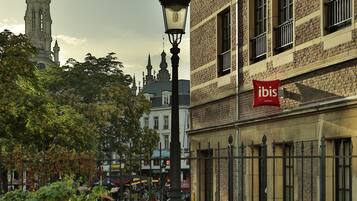 A hotel with a brick facade, a prominent 'ibis' sign, and a historic tower in the background.