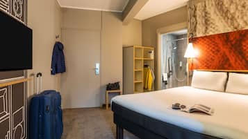 A hotel room with a bed, a suitcase, a coat rack, a wardrobe, and a shower area.
