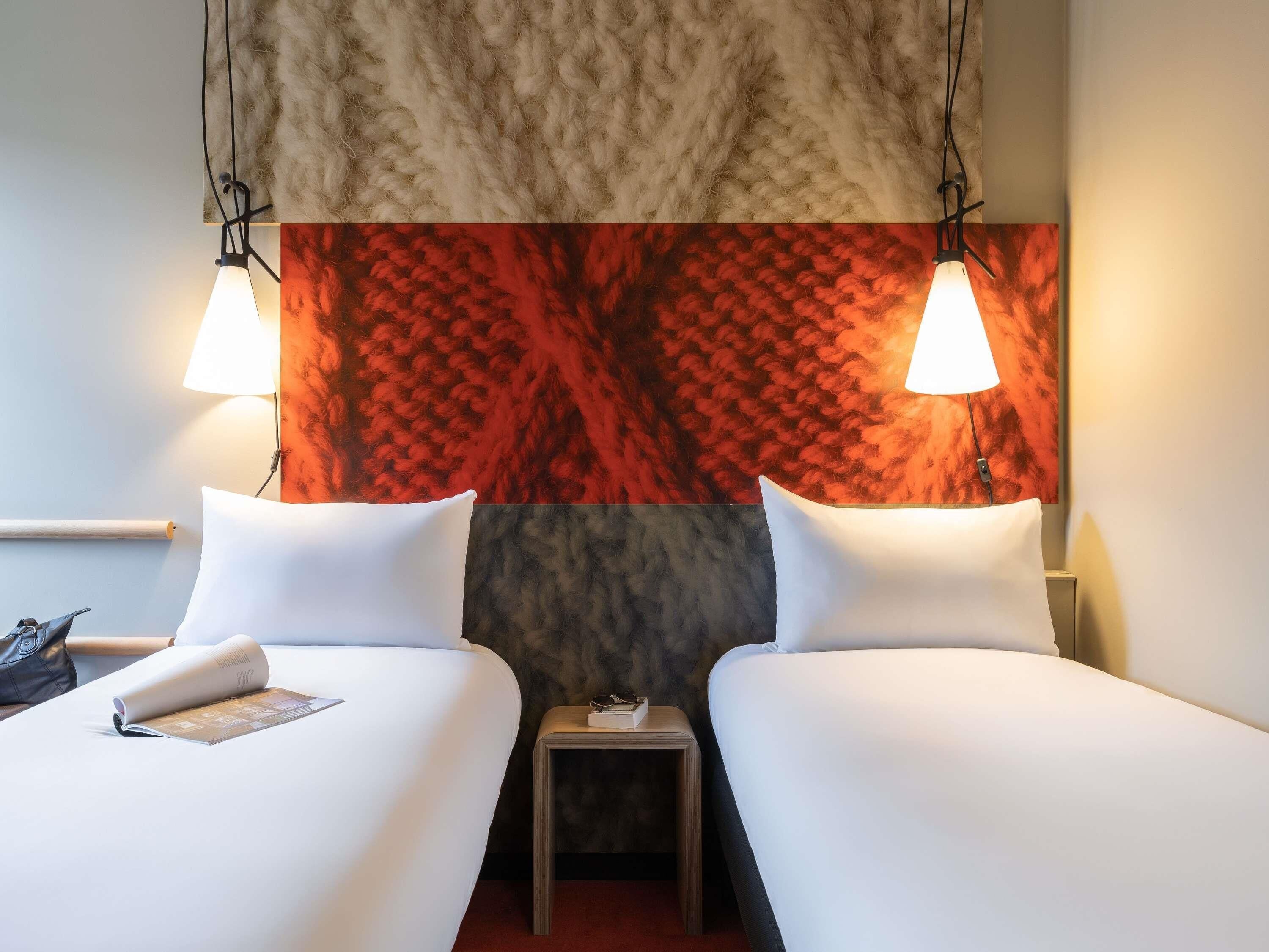A hotel room with two beds, a small table, and a nightstand.