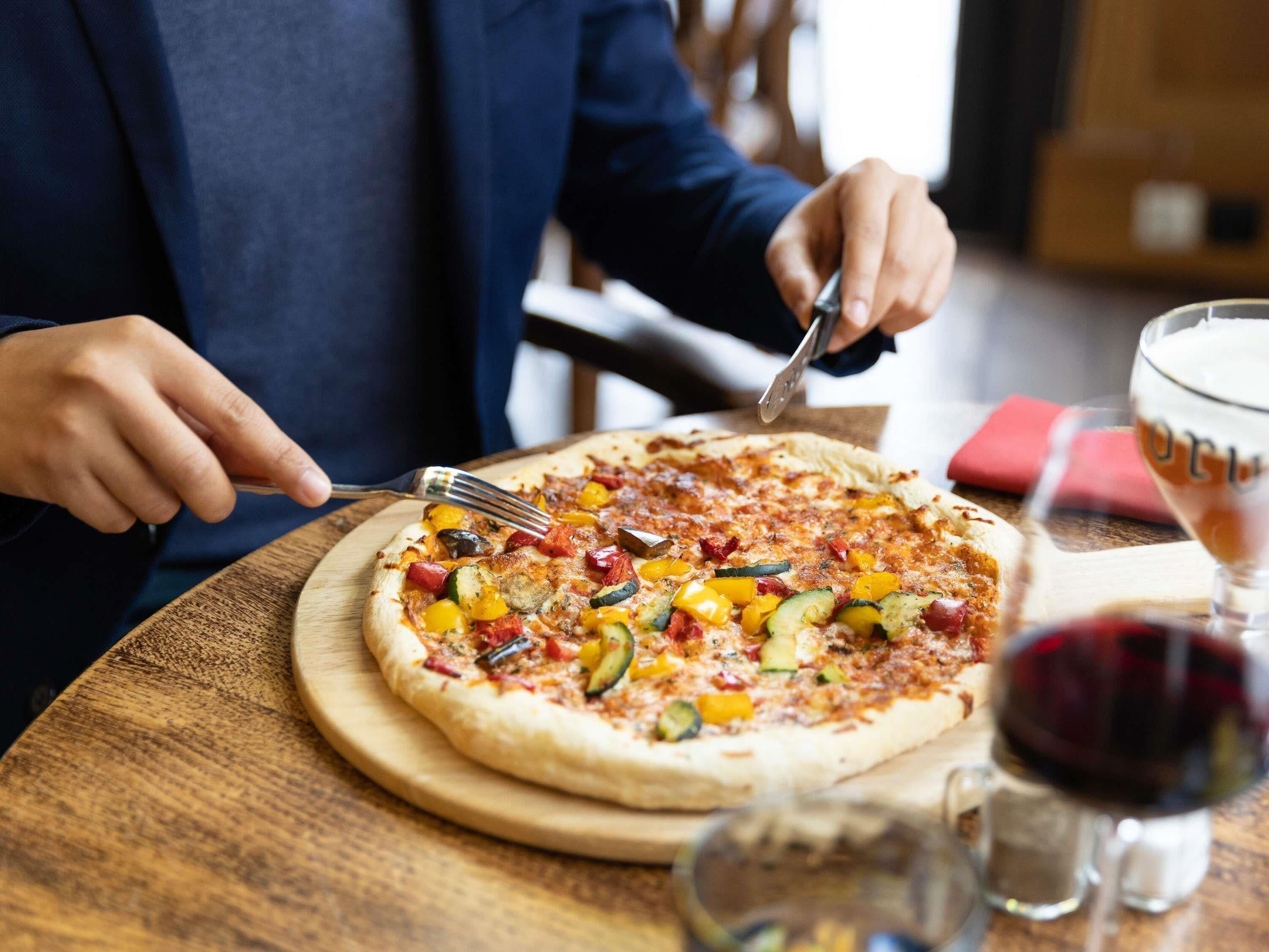 A person cutting a vegetable pizza on a wooden board.