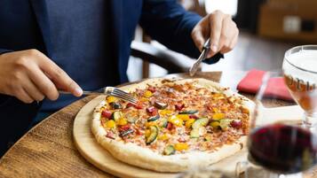 A person cutting a vegetable pizza on a wooden board.