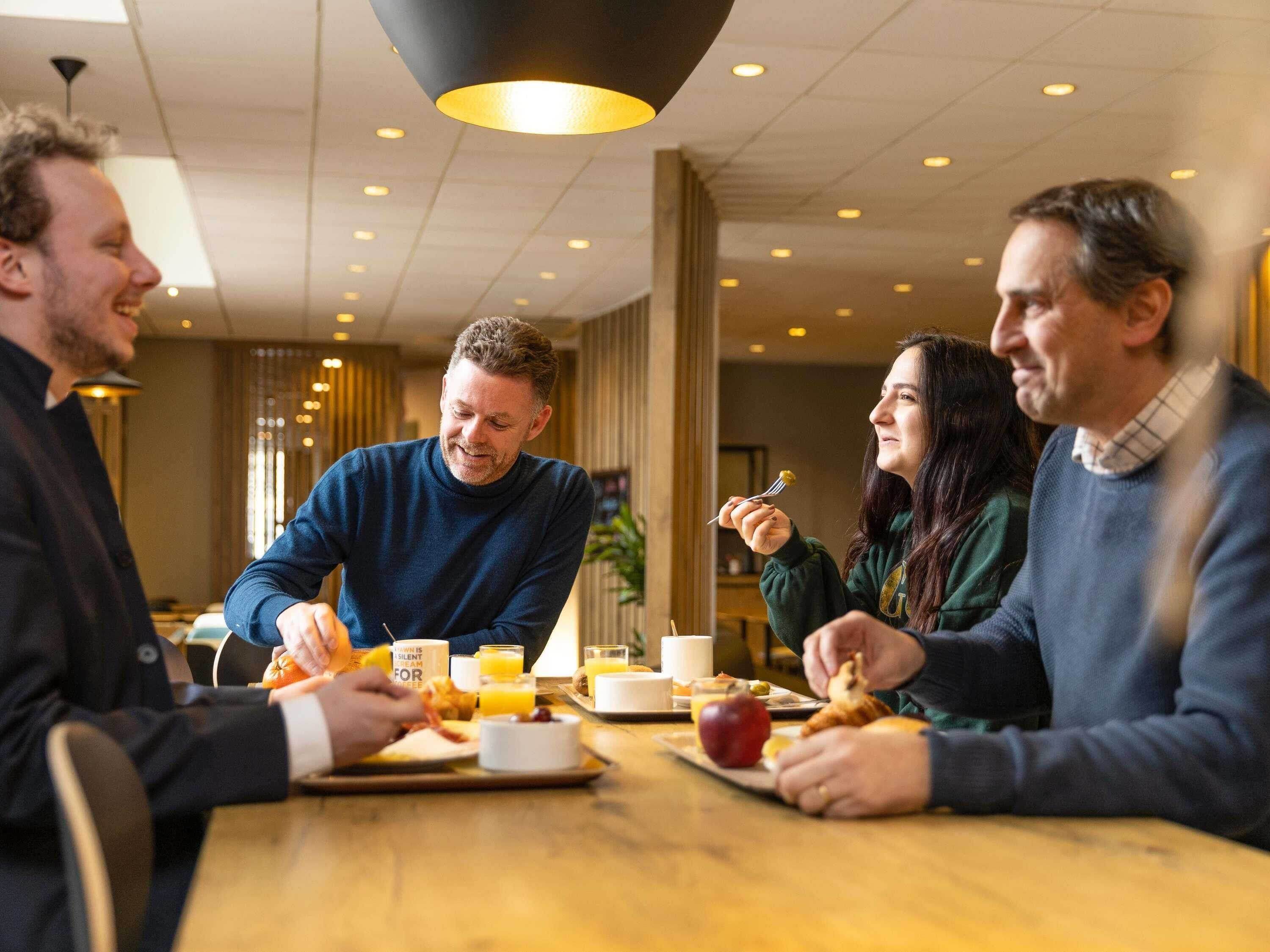 Eine Gruppe von Personen speist an einem Tisch in einem hell erleuchteten Innenraum mit modernem Deckenstil und indirekter Beleuchtung.