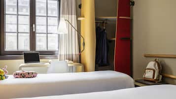 Een hotelkamer met een bed, een bureau met een laptop, een surfplank en een kledingkast.