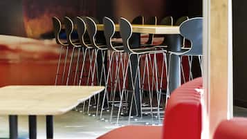 A restaurant interior with a wooden table, red upholstered seating, and hanging pendant lights.
