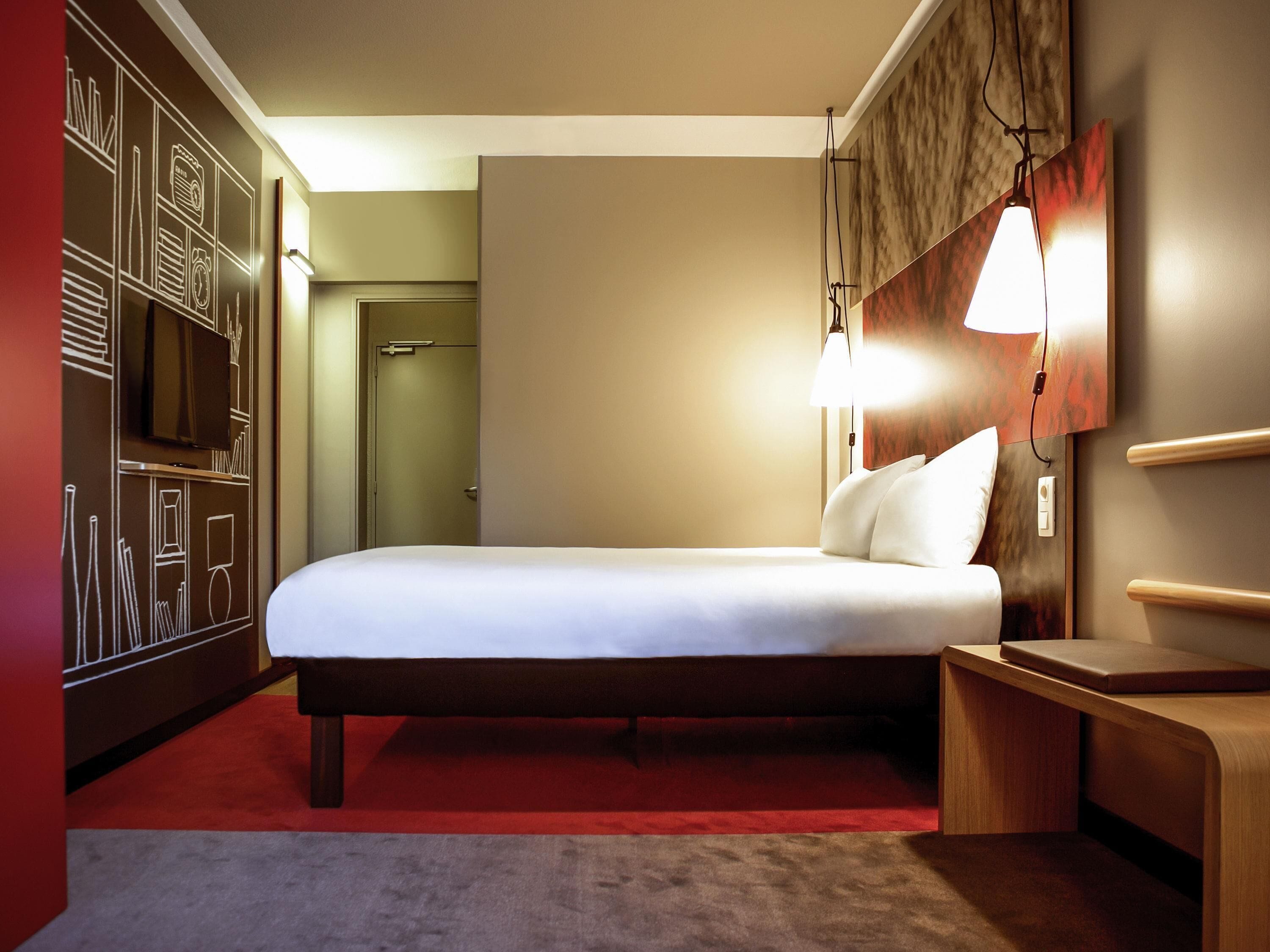 Ein Hotelzimmer mit Bett, Fernseher, Nachttisch und einer Wand mit abstrakten Designs.