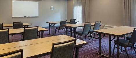 A conference room with multiple tables and chairs, a whiteboard, and a projector screen.