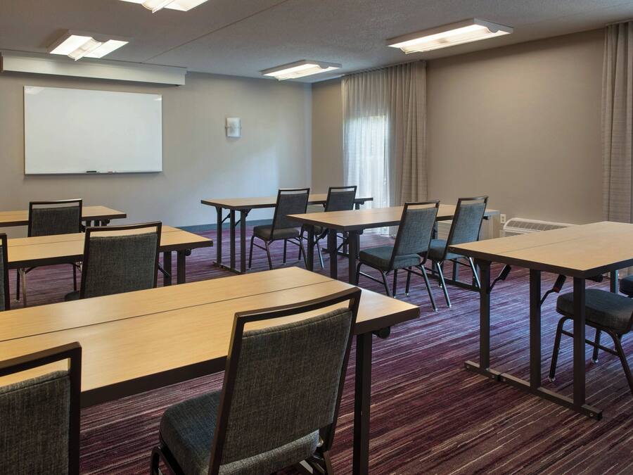 Un salón de conferencias con varias mesas y sillas, una pizarra y una pantalla de proyector.