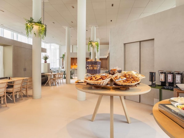 Un interior moderno con una mesa de buffet que exhibe diversas opciones de panadería, todo ello bajo altos techos e iluminación natural.