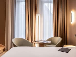 A hotel room with a bed, two armchairs, a small table with a magazine, and a floor lamp. - Novotel Brugge Centrum (Bruges)