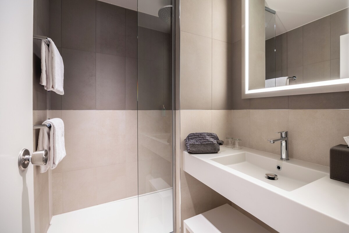 A modern bathroom with a glass shower enclosure, a white sink, and a large mirror.