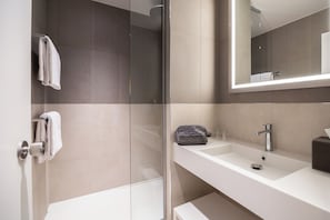 A modern bathroom with a glass shower enclosure, a white sink, and a large mirror. - Novotel Brugge Centrum (Bruges)