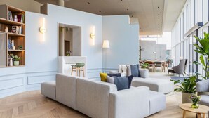 A modern living room with a sofa, a coffee table, and a bookshelf. - Novotel Brugge Centrum (Bruges)